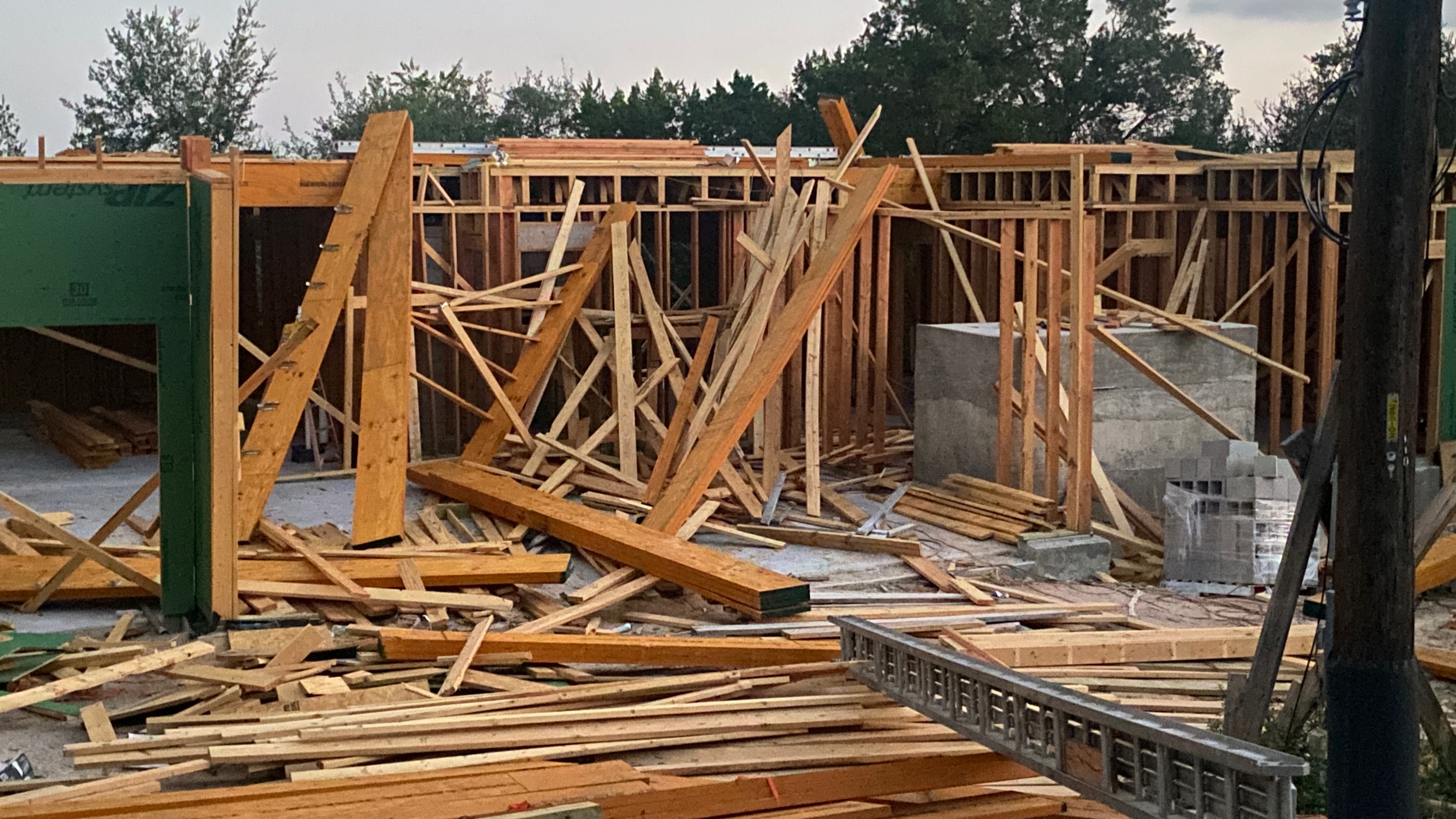 A wood-framed building left standing after a storm, with a large heap of blown-down loose lumber piled in front of it.